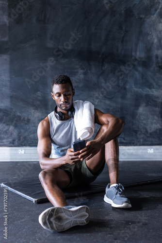 African American young male athlete sits in gym, holding a smartphone, copy space © wavebreak3