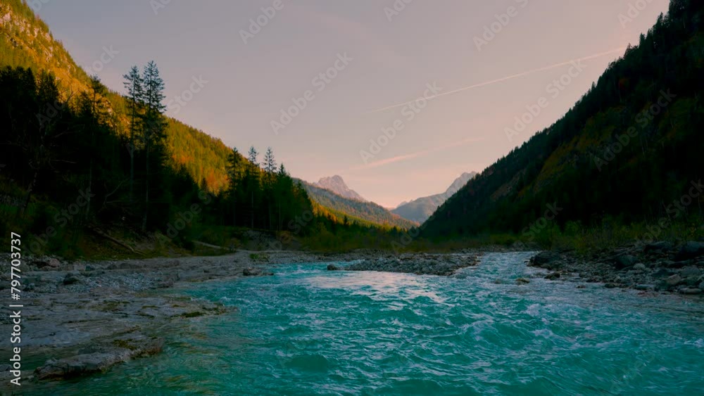 Mountain river evening, clear blue water rushing by vibrant colorful autumn trees in the sun. Austrian alps