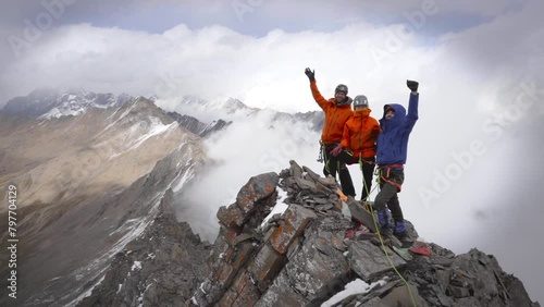 Group Of Trad Climbers Raising Hands In The Air On Cragged Mountain Peak. wide shot photo