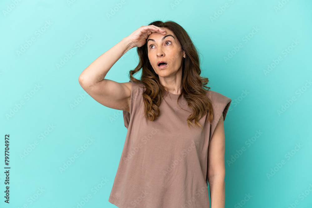 Middle aged caucasian woman isolated on blue background doing surprise gesture while looking front Middle aged caucasian woman isolated on blue background doing surprise gesture while looking front