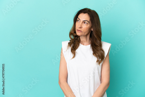 Middle aged caucasian woman isolated on blue background looking to the side © luismolinero