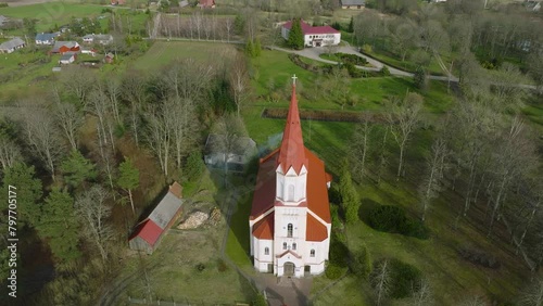 Aerial view of a white church with red roof (Rucava Lutheran Church, Rucava, Latvia) on a sunny spring day, wide angle drone orbit shot photo