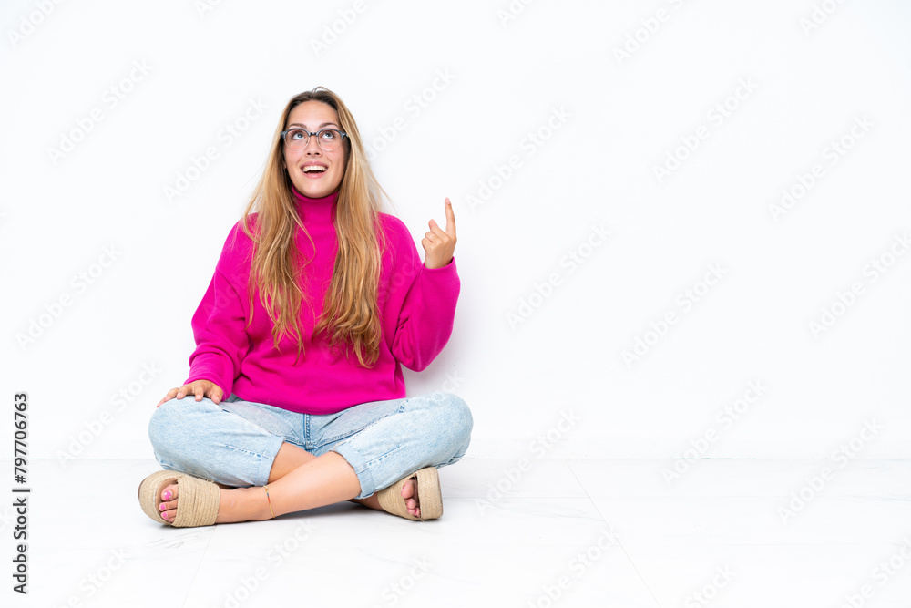 Young caucasian woman sitting on the floor isolated on white background pointing up and surprised Young caucasian woman sitting on the floor isolated on white background pointing up and surprised