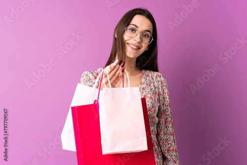 Young woman over isolated purple background holding shopping bags and thinking