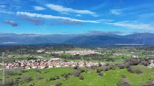 lateral flight with a drone in the valley where we see a rural town, a green area of ​​pasture with cattle and in the background the central peninsular mountain system with a blue sky with clouds photo