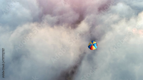 Colorful parachute is soaring through the cumulus clouds in the electric blue sky, carried by the wind in a mesmerizing meteorological phenomenon