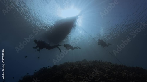 Backlight shot of scuba divers under a diving boat in clear blue water next to a tropical coral reef silhouette beauty shot at the island of Tahiti, French Polynesia photo