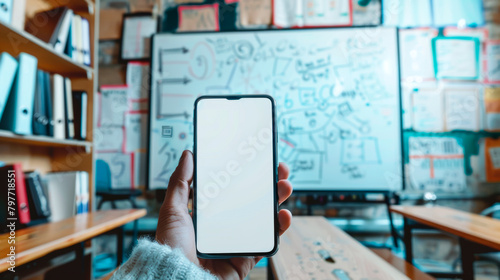 Hand holding a smartphone with a blank screen in front of a whiteboard with flowcharts