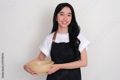 An Asian woman wearing apron smiling while holding empty big serving bowl photo