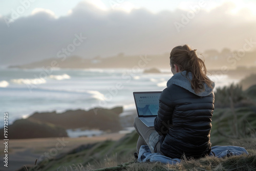 Serene coastal scene with woman focused on laptop screen.