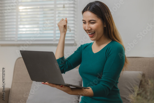 a beautiful Asian teenage girl is having fun watching entertainment in  an application on laptop at home on the sofa, a beautiful female spend a weekend on the couch in ultimate bliss in an apartment.
