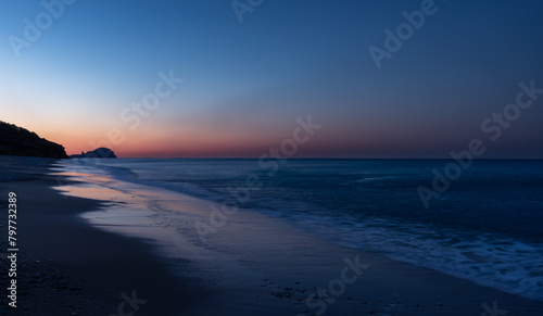 Sunrise at the Yanışlı beach on the background of  reddish sky and waves wash ashore of the Mediterranean Sea at the long exposure photo