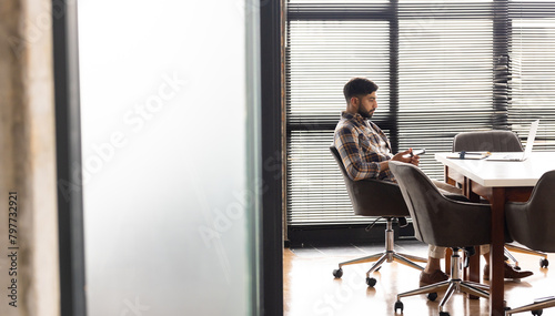 Asian young professional man sitting alone at a conference table in a modern business office, lookin photo