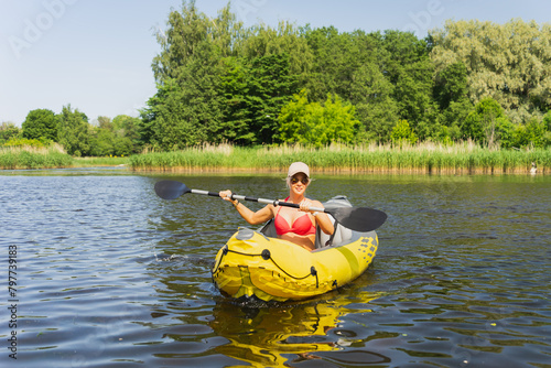 A young girl in sunglasses is kayaking on the river on a summer day.