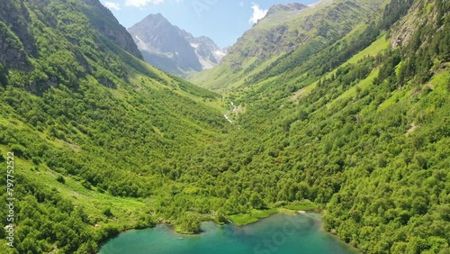 Flying back over a forest and lake with turquoise water among the mountains in sunny weather. Ahead is a green valley between the mountains. 4K. photo