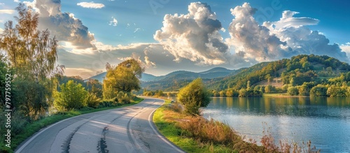 Beautiful view of rural road and green trees with sky clouds by the lake. Generated AI image