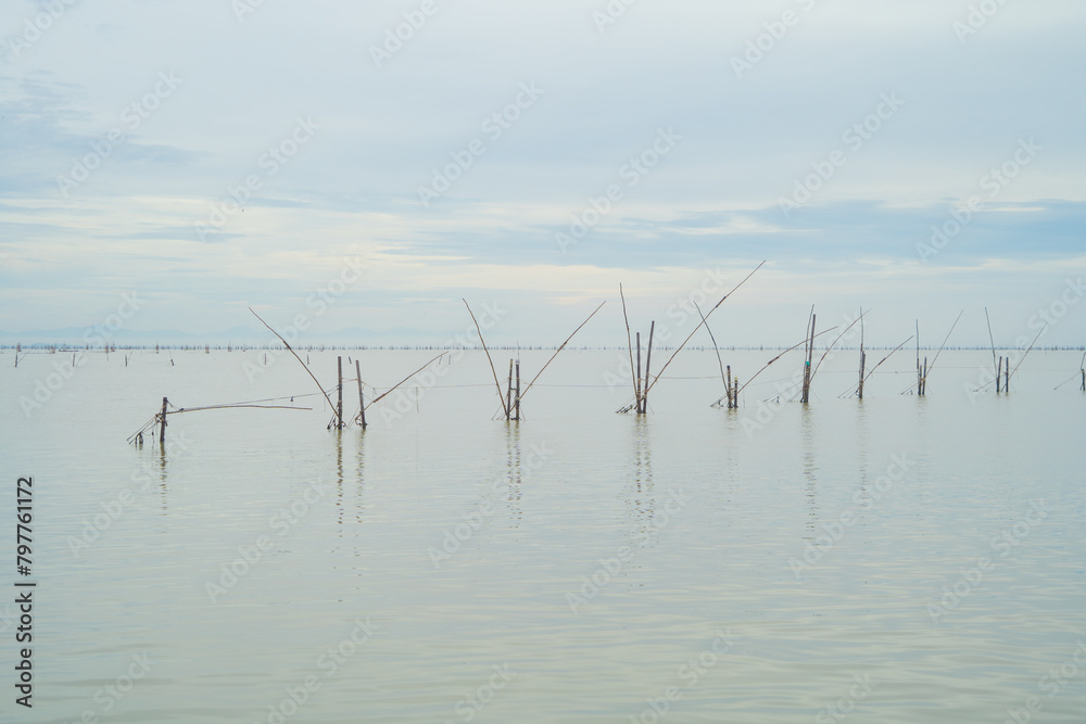 Fototapeta premium Fishing trap net in canal with fisherman urban city village town houses, lake or river. Nature landscape fisheries and fishing tools at Pak Pha, Songkhla, Thailand. Aquaculture farming