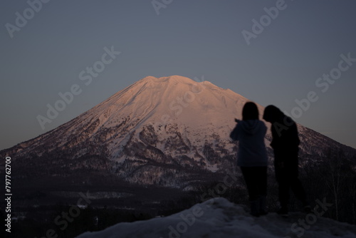 Silhouette of two individuals gazing at snowy Mount Yotei in Niseko, Japan. © Wirestock