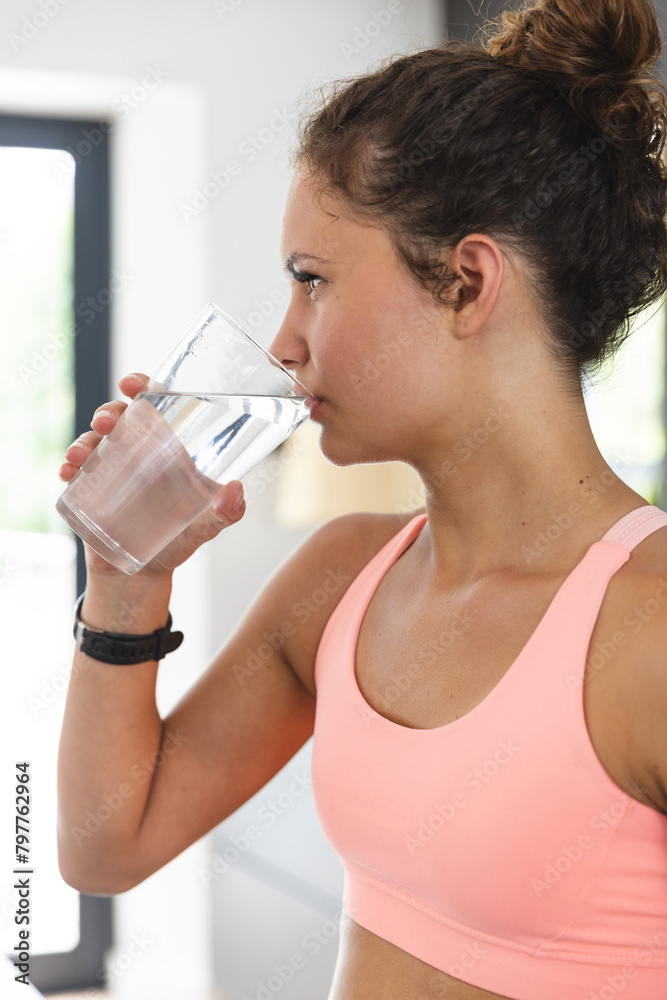 A young fit Caucasian woman wearing pink top, drinking water