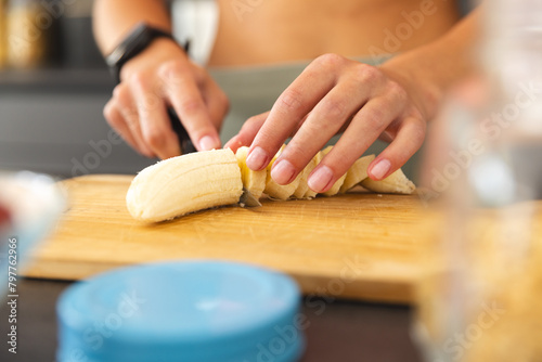A young Caucasian woman slicing banana on cutting board at home photo