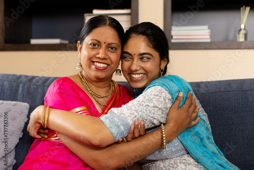 Indian mother and teenage daughter, wearing traditional clothes, hugging at home photo