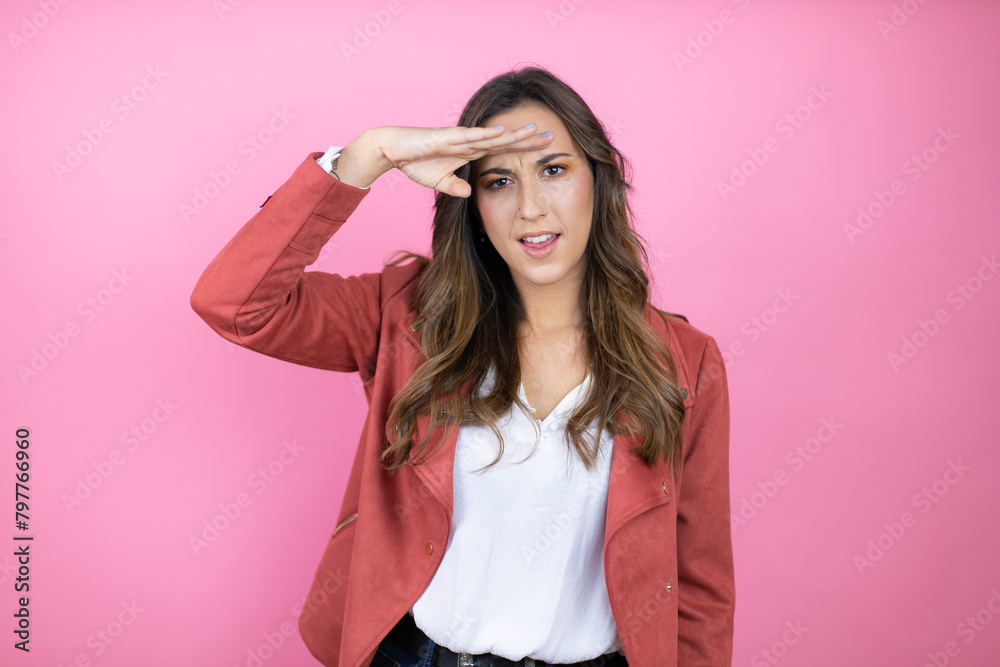 Young beautiful woman wearing casual jacket over isolated pink background very happy and smiling looking far away with hand over head. searching concept. Young beautiful woman wearing casual jacket over isolated pink background very happy and smiling looking far away with hand over head. searching concept.