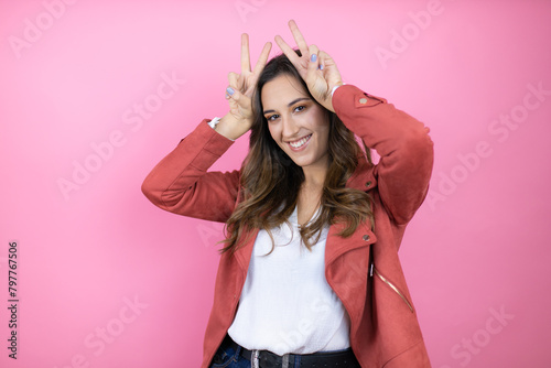 Young beautiful woman wearing casual jacket over isolated pink background Posing funny and crazy with fingers on head as bunny ears, smiling cheerful photo