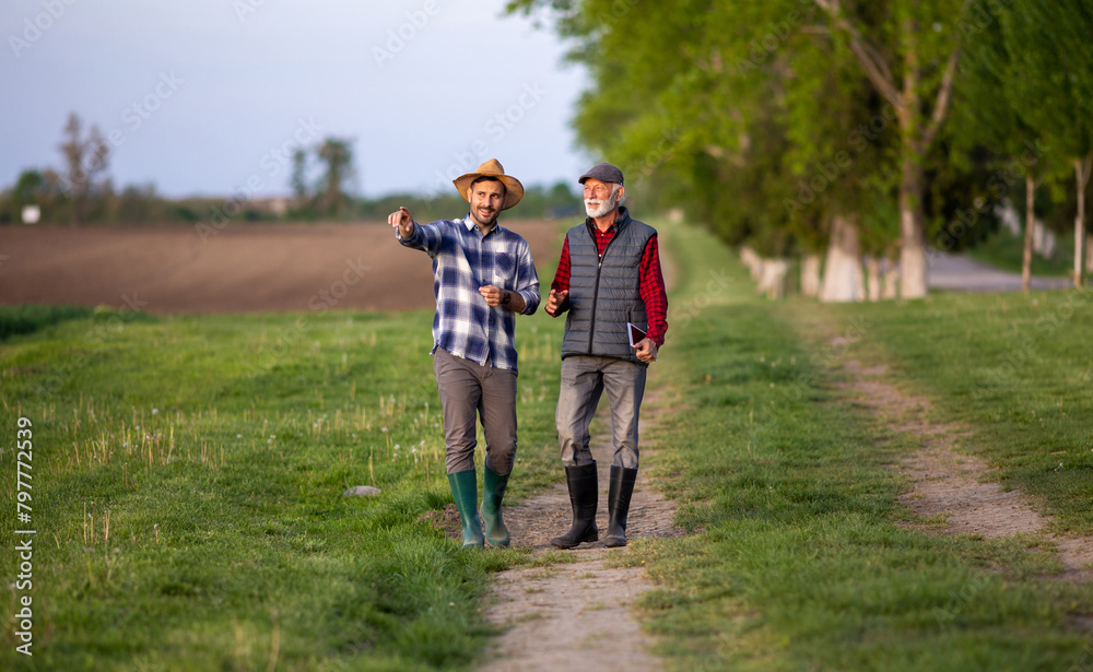 Two farmers walking and discussing on dirt road in field