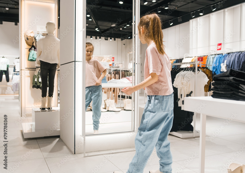 Young Girl Trying on Clothes and Looking at Mirror in Clothing Store Young Girl Trying on Clothes and Looking at Mirror in Clothing Store