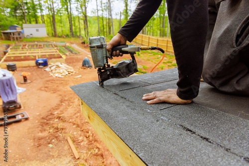 Installing new asphalt bitumen shingles to roof with pneumatic air nail gun