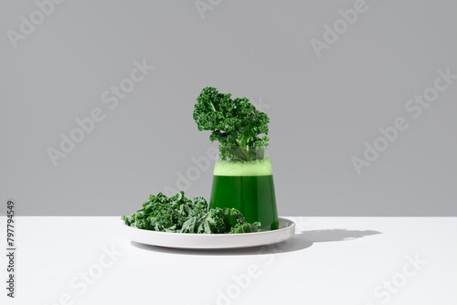 Batido de desintoxicación de jugo de col rizada verde y hojas frescas de col rizada en un plato blanco sobre fondo gris	 photo