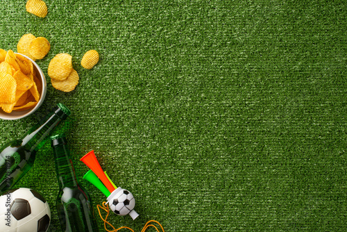 Football fan's feast. Overhead shot of game day treats: crunchy tortilla chips, chilled beer, soccer ball, themed accessories, and pipe, on grass with empty text space