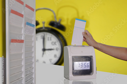 A time clock with a clock behind it and a hand punching in.