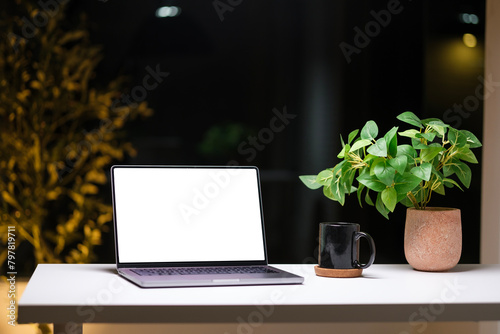 Laptop and office supplies on white table in modern dark home office at night.