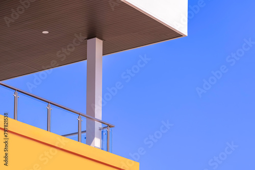 Modern house balcony with glass baluster and wooden ceiling roof against blue sky background, low angle and perspective side view