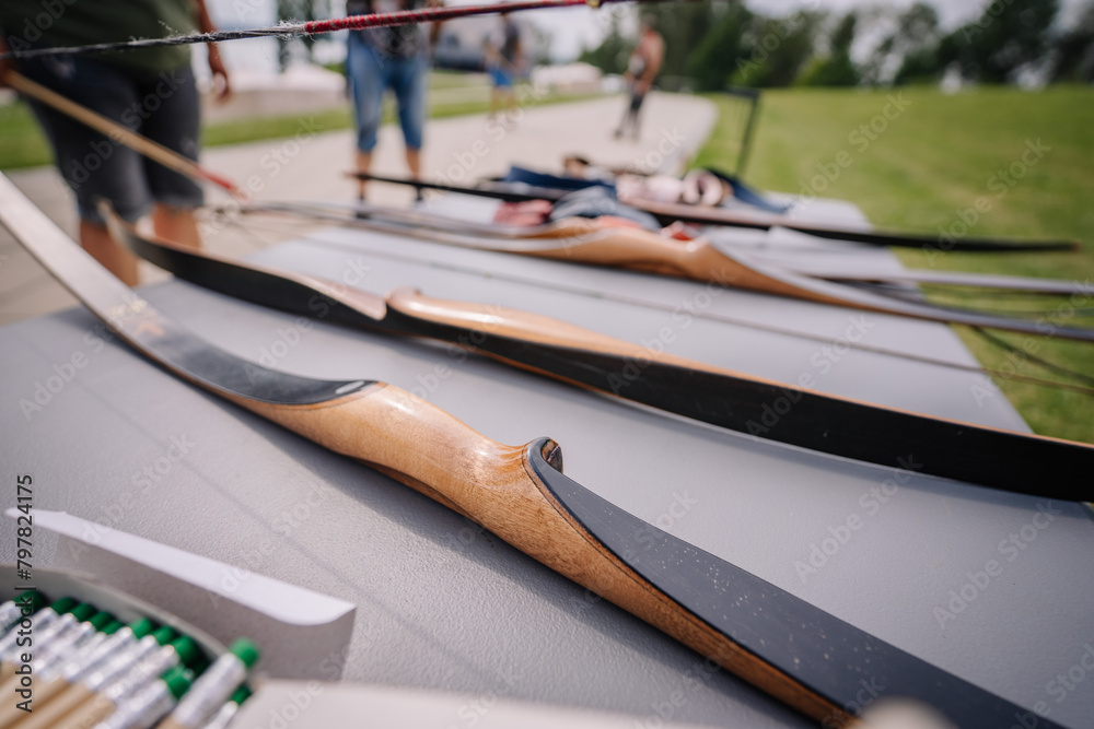 Dobele, Latvia - August 18, 2023 - Close-up of a row of traditional wooden archery bows on a table, with arrows and other equipment in the background.