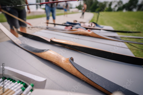 Dobele, Latvia - August 18, 2023 - Close-up of a row of traditional wooden archery bows on a table, with arrows and other equipment in the background. photo