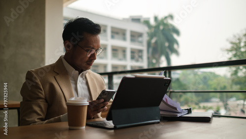 Millennial businessman using mobile phone and working with digital tablet. © wattana