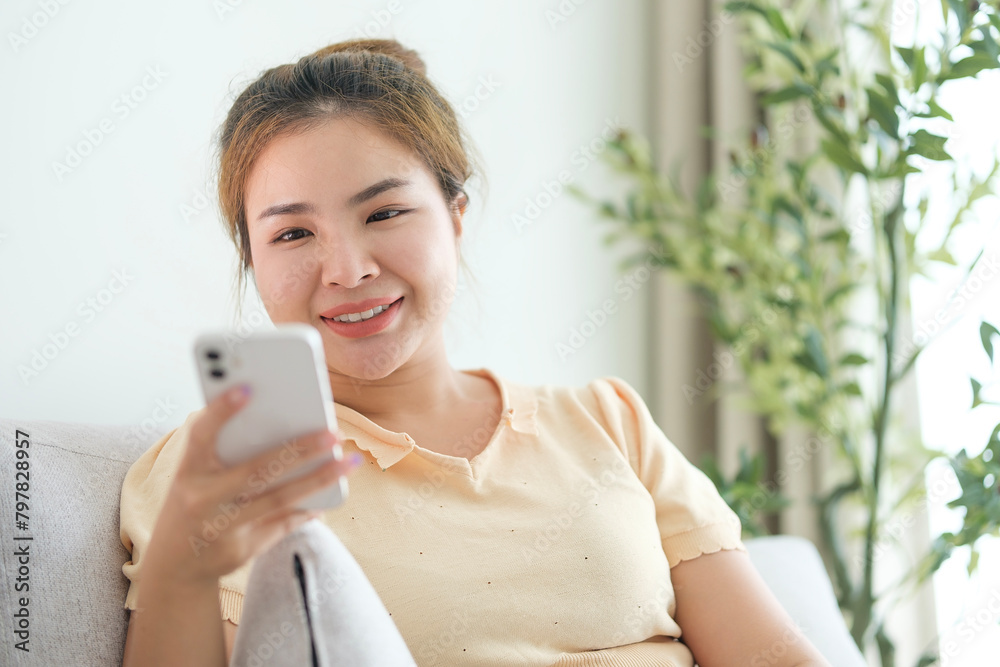 Smiling young woman checking social media on her mobile phone at home. People and technology concept. Smiling young woman checking social media on her mobile phone at home. People and technology concept.