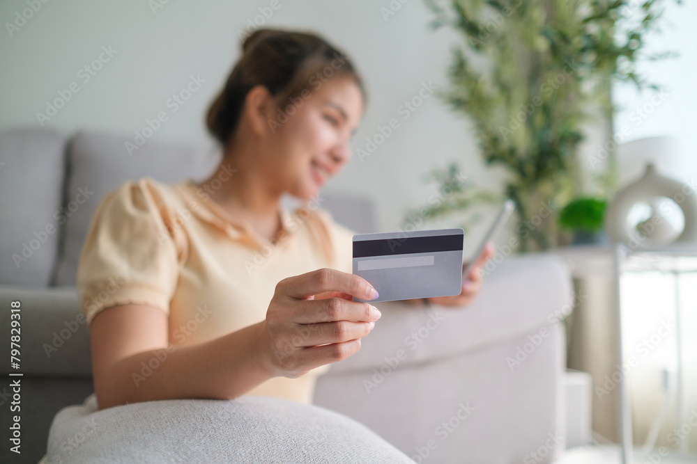 Happy young woman holding credit card and mobile phone while paying bill or shopping online at home. Happy young woman holding credit card and mobile phone while paying bill or shopping online at home.