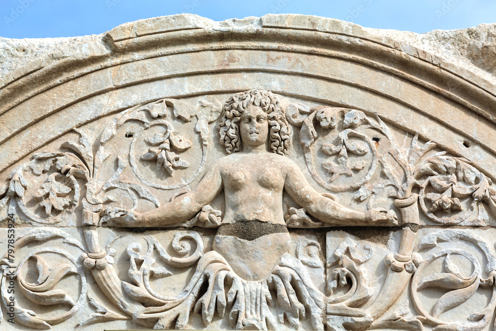 Close-up of a Medusa relief on the arch of Hadrian's Temple in Ephesus, under a bright sky. Selcuk, Izmir, Turkey (Turkiye)