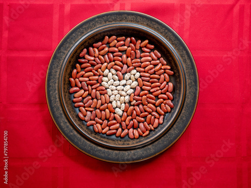A Heart made out of Healthy Pinto Beans in a field of Kidney Beans, arranged on a Brown Plate on a Red tablecloth.