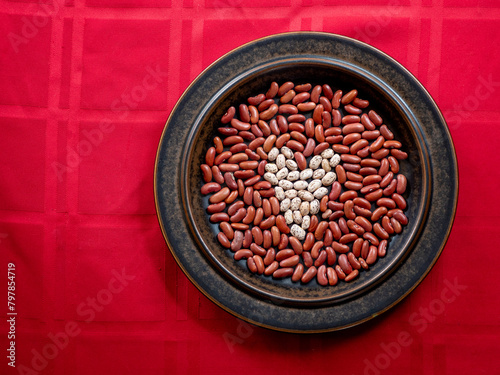 A Heart made out of Healthy Pinto Beans in a field of Kidney Beans, arranged on a Brown Plate on a Red tablecloth.