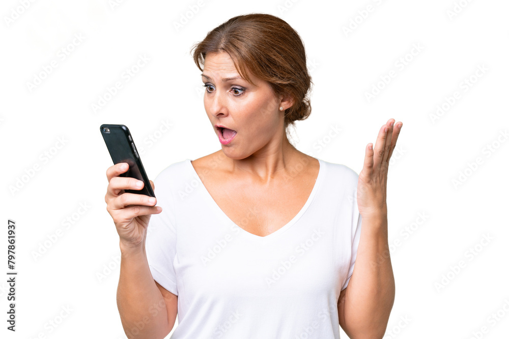 Middle-aged caucasian woman over isolated background looking at the camera while using the mobile with surprised expression Middle-aged caucasian woman over isolated background looking at the camera while using the mobile with surprised expression
