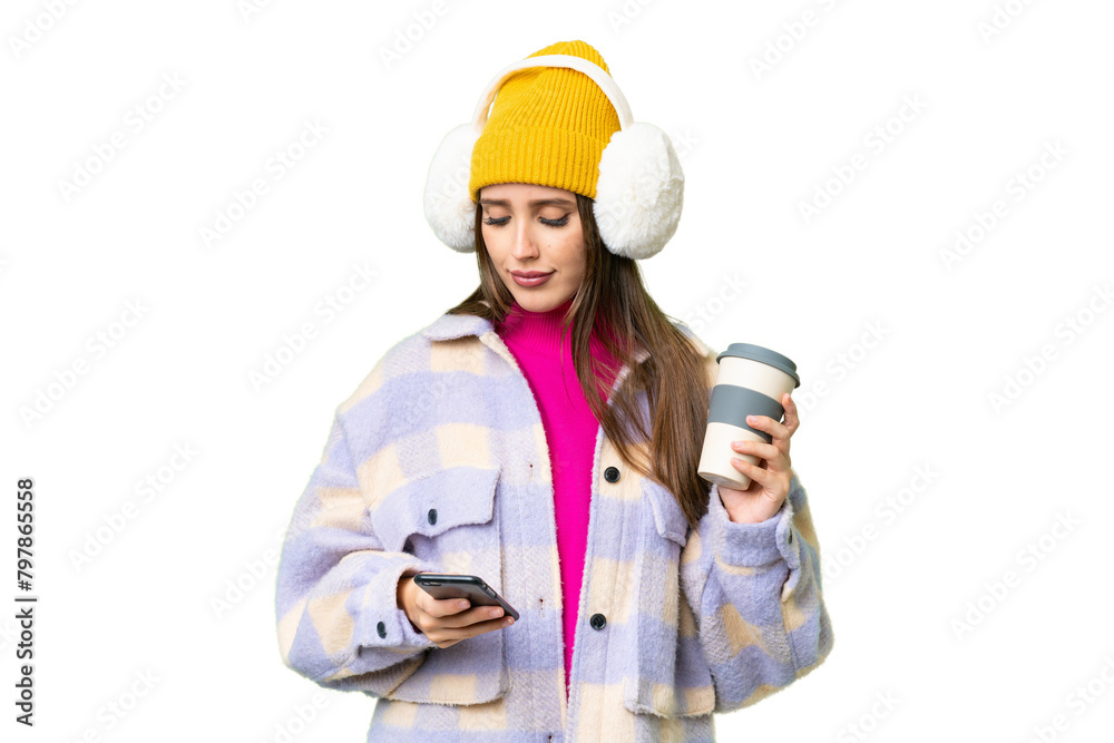 Young woman wearing winter muffs over isolated chroma key background holding coffee to take away and a mobile
