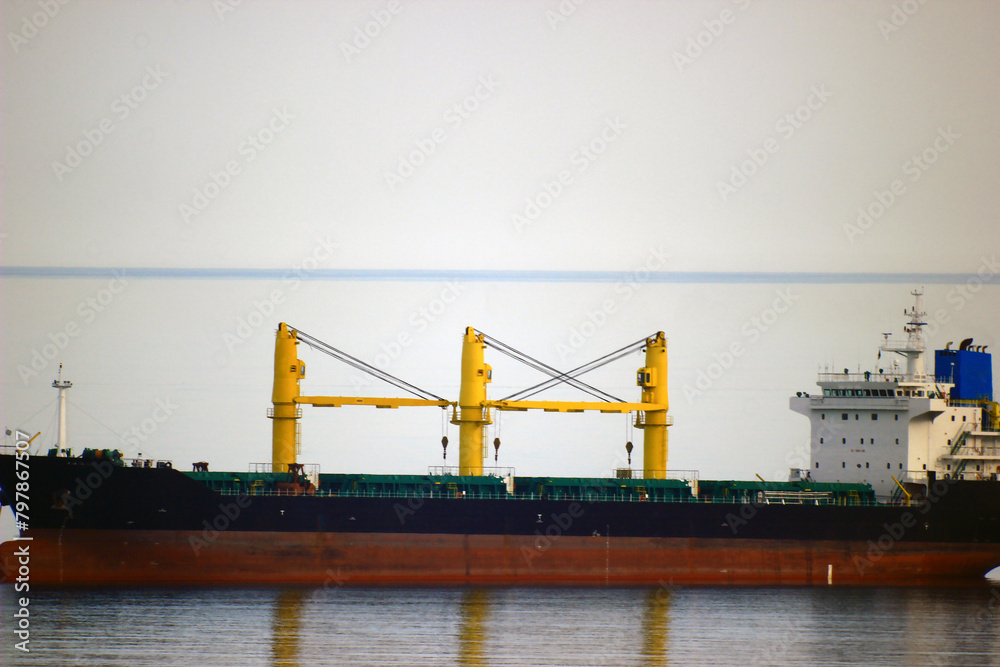 A large ship with yellow cranes is reflected in sea water