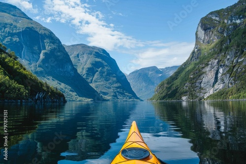 Sunny day view from a kayak gliding through calm waters of Norwegian fjords with towering mountains either side