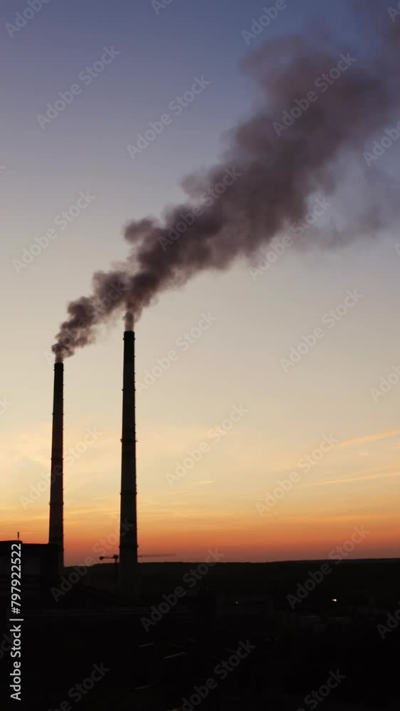 Dark background of plant with industrial pipes. Smokestacks of the plant against the background of an orange sunset. Bad ecological situation. Air pollution. Vertical video