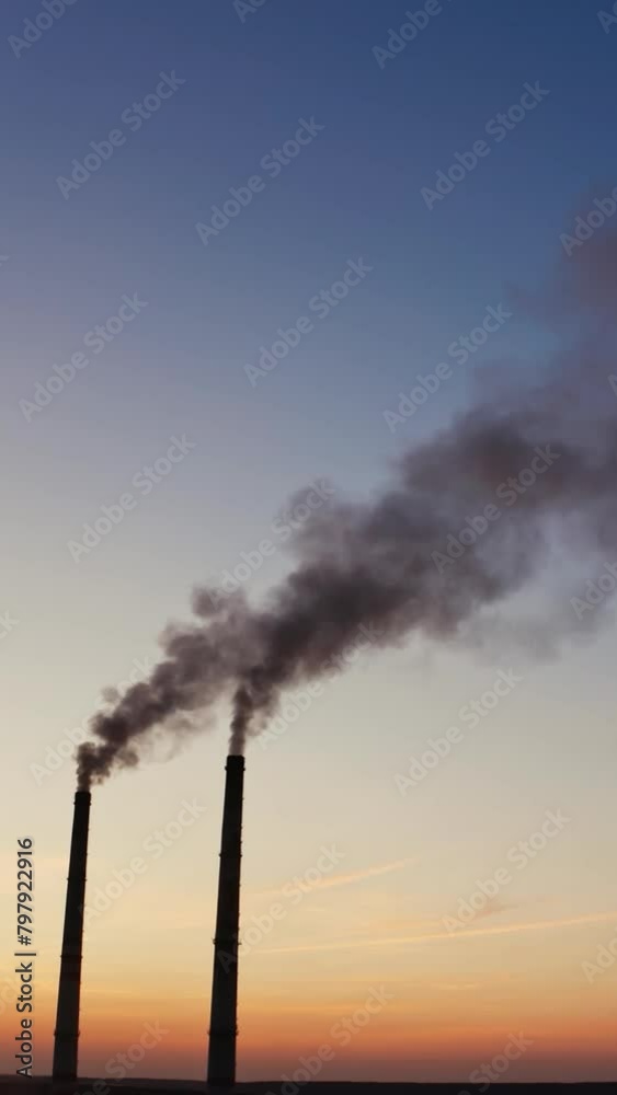 Pollution of the environment.Toxic smoke going from two pipes of a factory on the evening sky background at sunset. Vertical video Pollution of the environment.Toxic smoke going from two pipes of a factory on the evening sky background at sunset. Vertical video