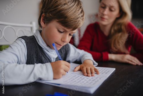 Boy pupil doing his homework at home with his mother